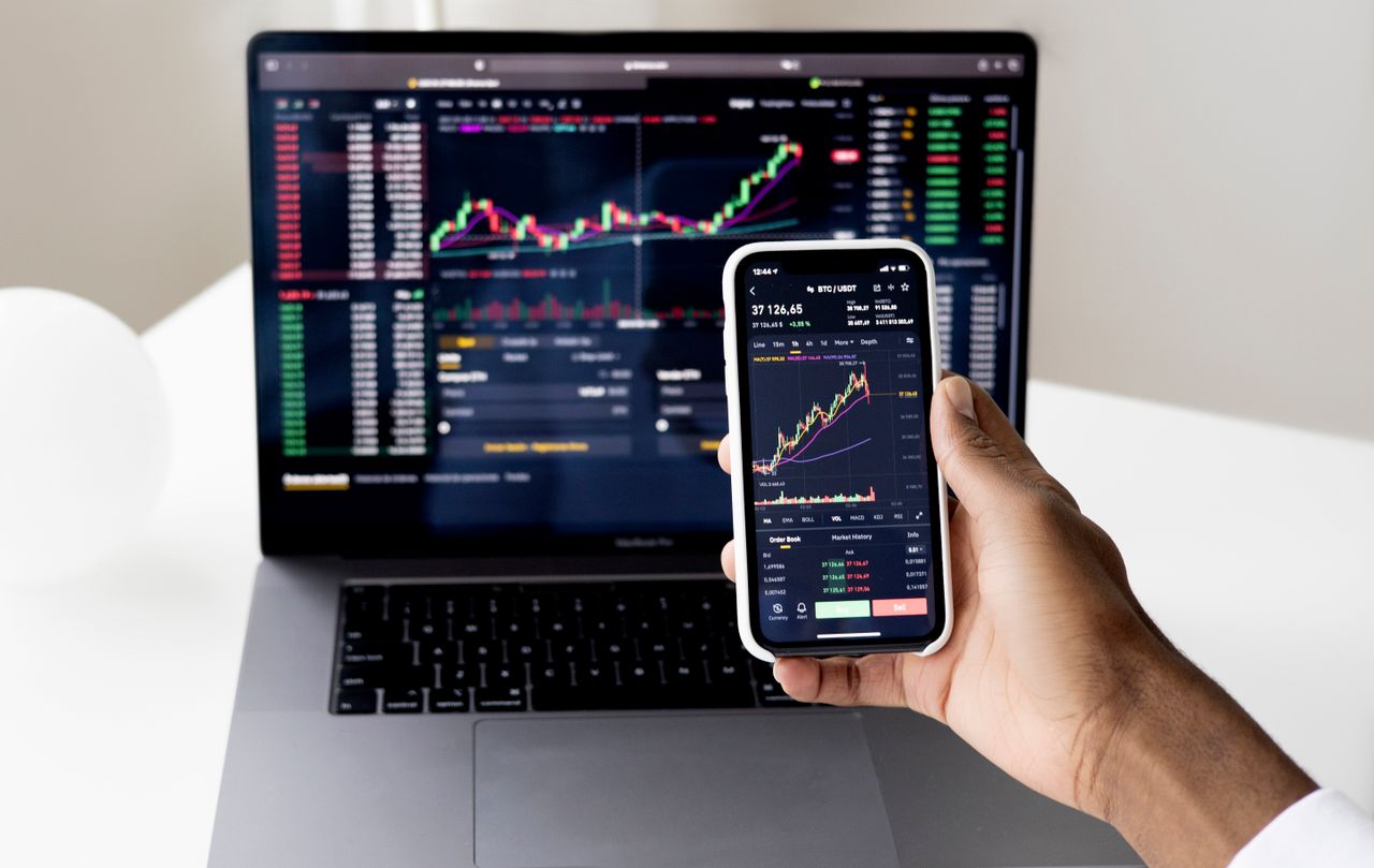 team-04 Person checking stock market graphs on laptop and smartphone, focusing on financial data.