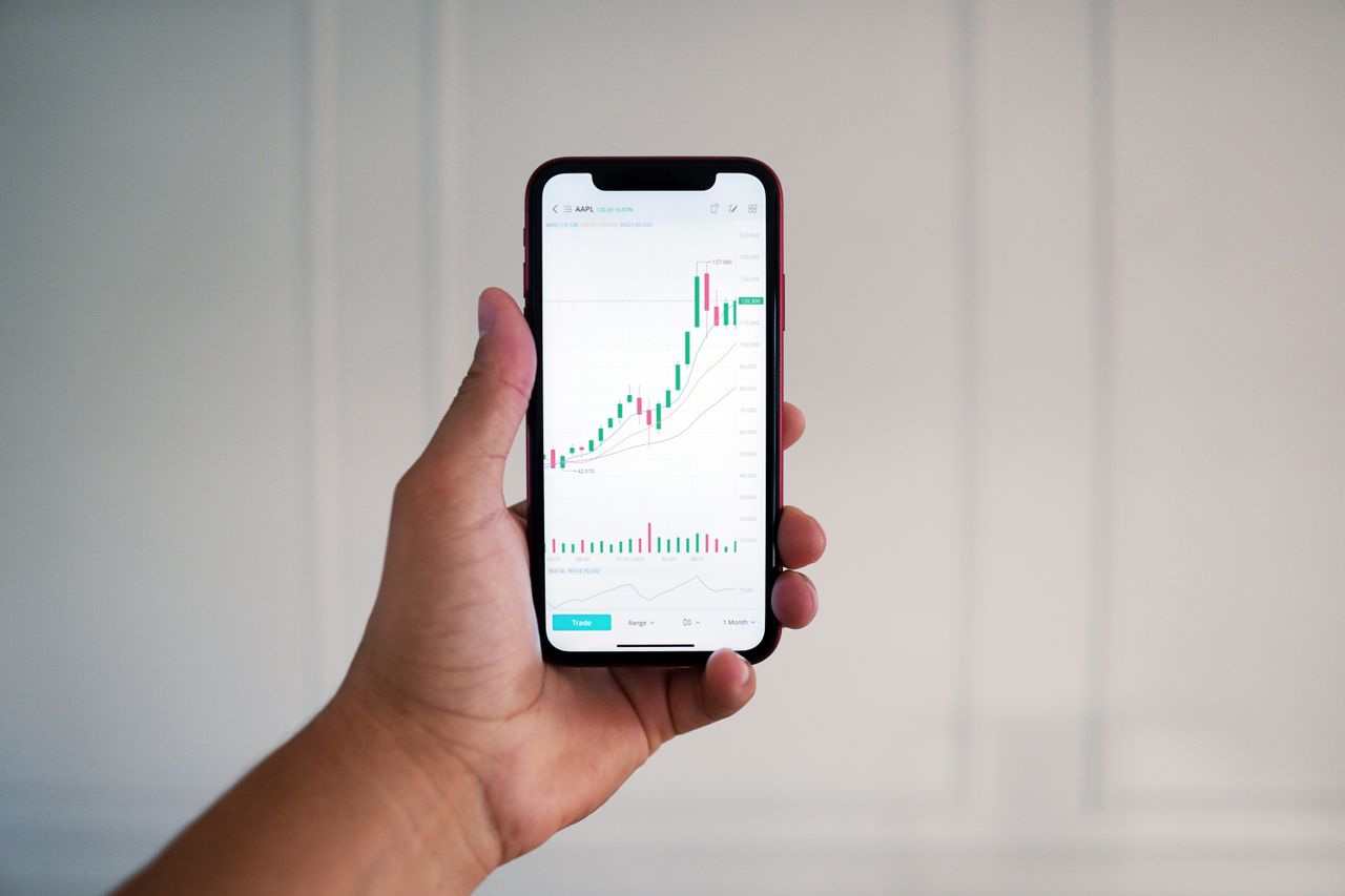 services-02 Close-up view of a hand holding a smartphone that displays a stock market chart indoors.